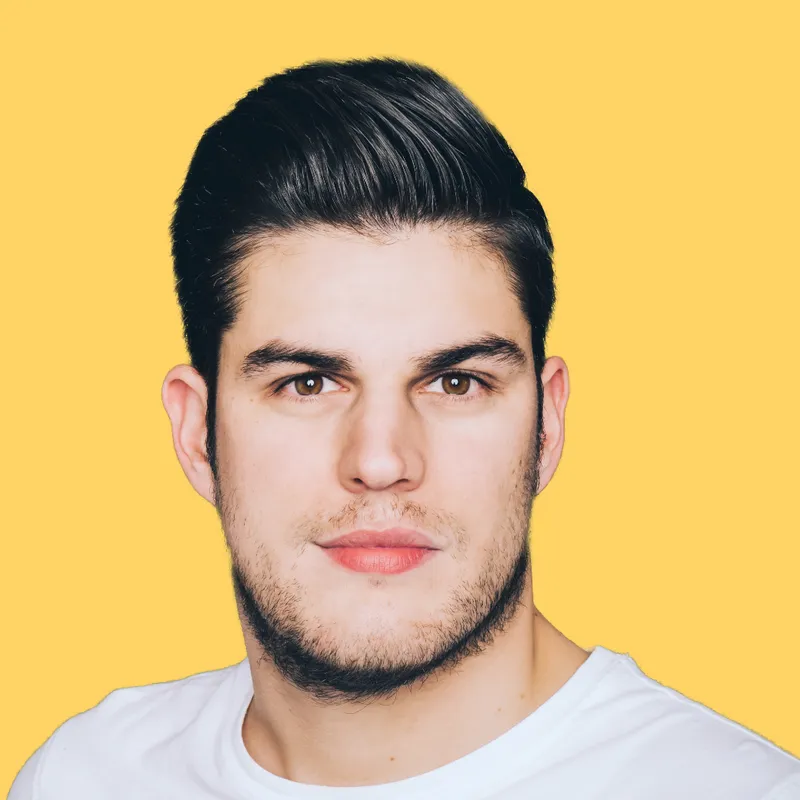 Mann mit kurzem, dunklem Haar und Bart, trägt ein weißes T-Shirt, vor einem gelben Hintergrund.