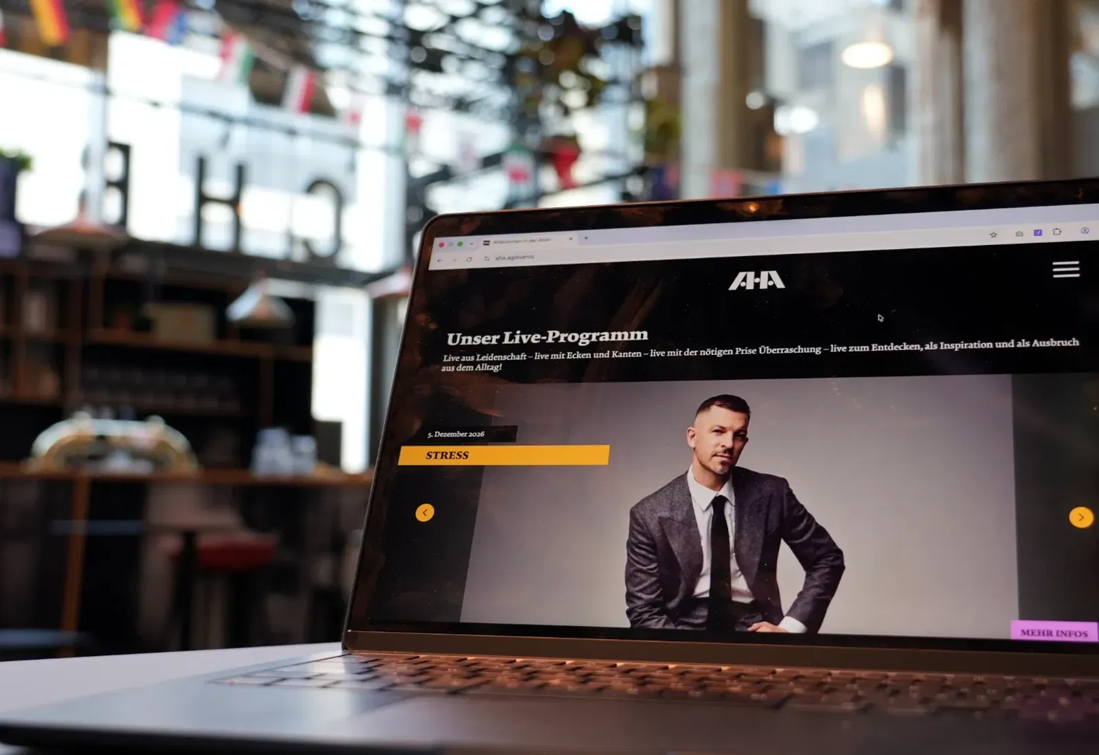 Laptop mit geöffneter Live-Programmseite, Moderator im Bild; unscharfer Hintergrund mit Regalen und Arbeitsumgebung in einem Büro.