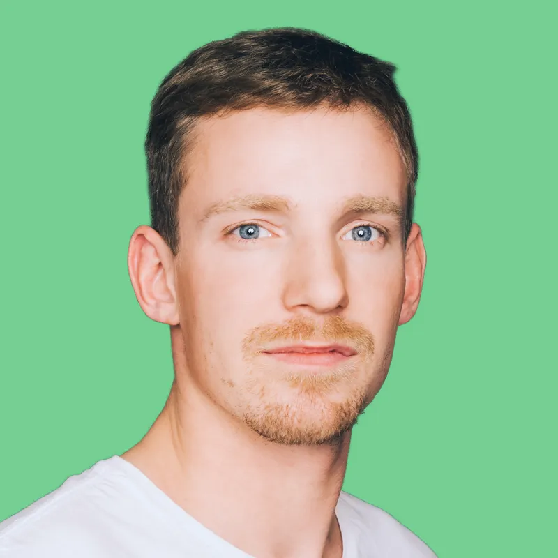 Mann mit kurzen, braunen Haaren und blauen Augen, trägt ein weißes T-Shirt, vor einem grünen Hintergrund.