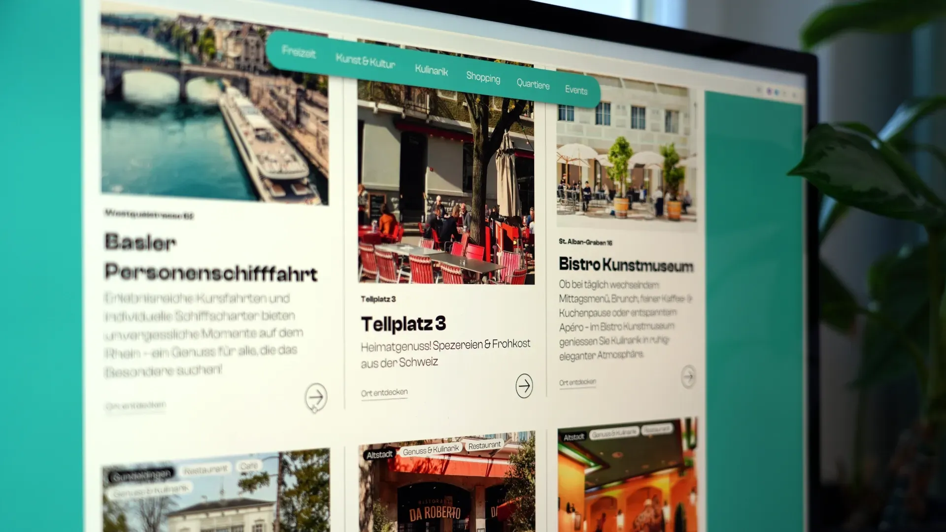 Tablet/Monitor mit Website-Übersicht: Kachelbereiche zu „Basler Personenschifffahrt“ und „Bistro/Kunstmuseum“, Menüleiste oben, Hintergrund mit Wasseransicht und Straßenansicht.