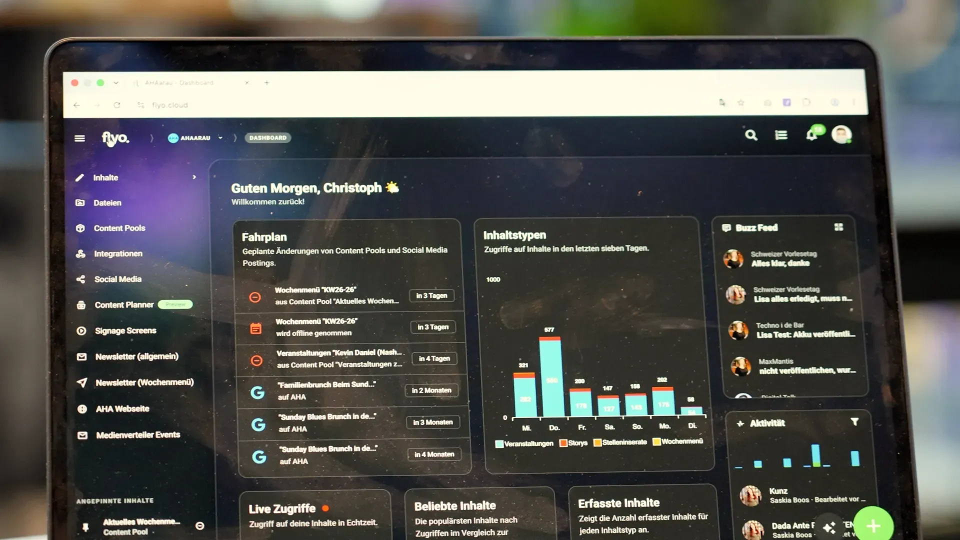 Ansicht eines Laptops mit Dashboard-Software: Menü links, zentrale Kacheln mit Diagrammen und Text, rechte Seitenleiste mit Kommentaren, unscharfer Hintergrund.