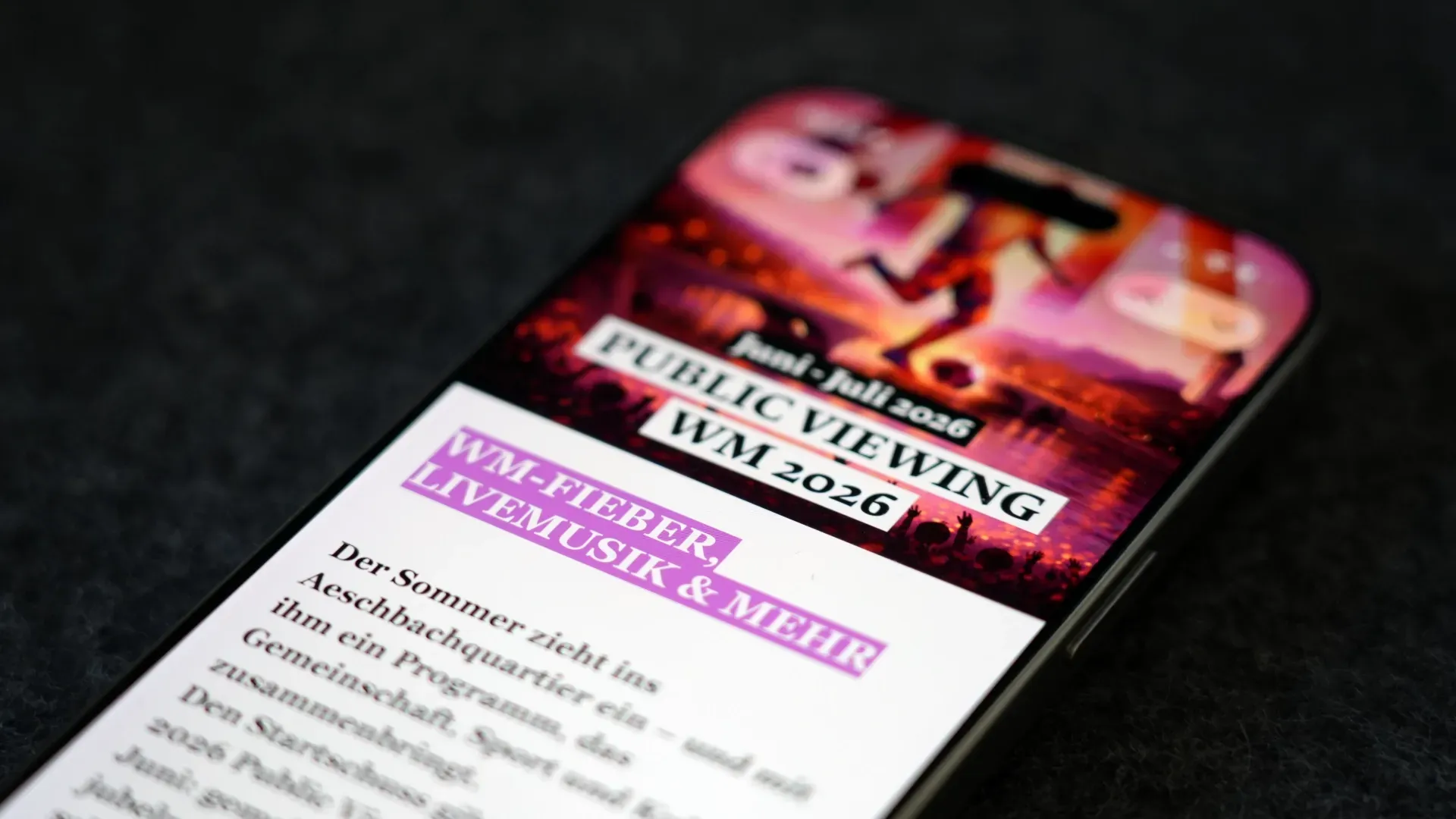 Smartphone mit Eventflyer „Public Viewing WM 2026“, „Wieder, Wm-Fieber, Live Musik & mehr“ und Datum 2026 auf weißem Bildschirm, im Hintergrund dunkler Stoff.
