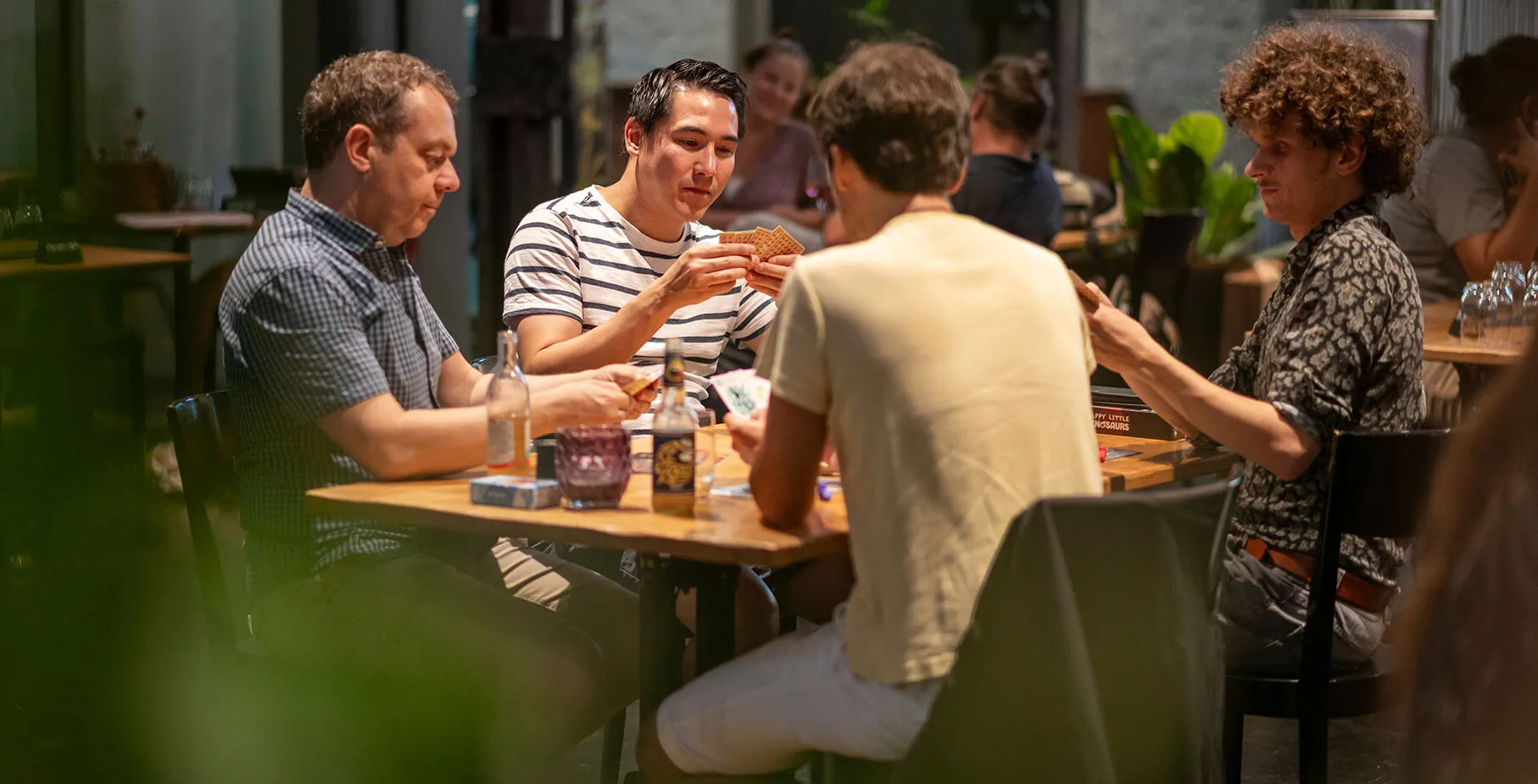 Vier Männer die an einem Tisch spielen und mit einem Bier oder Getränk ein Kartenspiel spielen