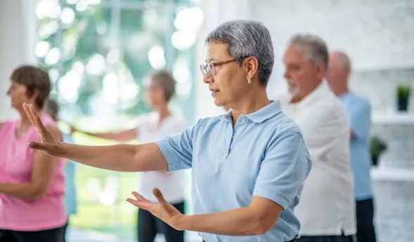 A group of seniors spend an afternoon indoors in a health center. They are doing group tai chi together.