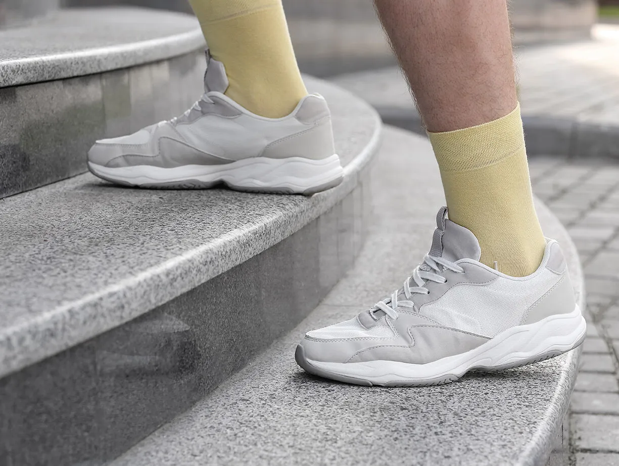 Graue Sportschuhe auf einer steinernen Treppe, kombiniert mit gelben Socken.