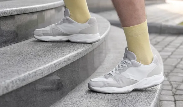 Graue Sportschuhe auf einer steinernen Treppe, kombiniert mit gelben Socken.