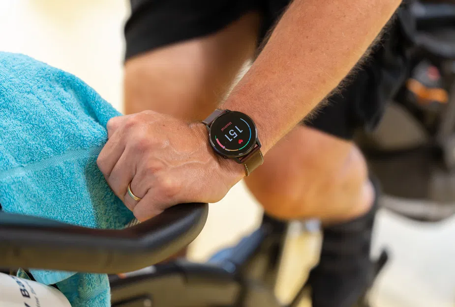 Person mit Smartwatch hält einen Lenker am Fitnessgerät; blaues Handtuch liegt darüber.