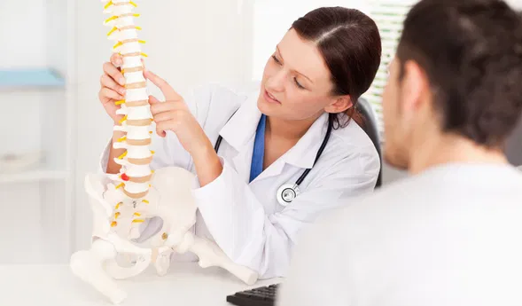 Ärztin erklärt einem Patienten anhand eines Wirbelsäulen- und Beckenmodells die Anatomie.