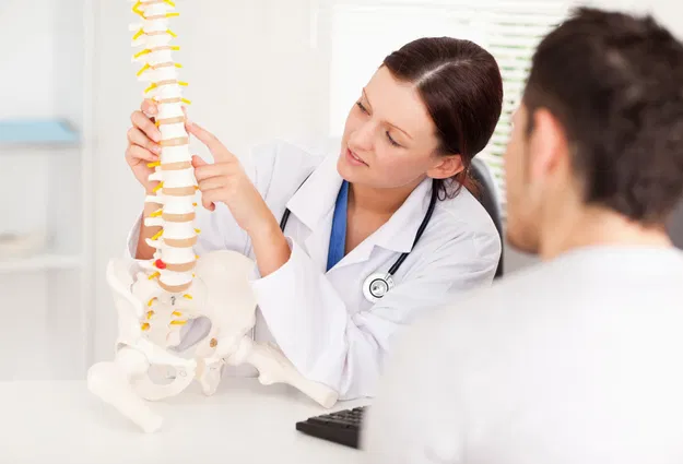 Ärztin erklärt einem Patienten anhand eines Wirbelsäulen- und Beckenmodells die Anatomie.