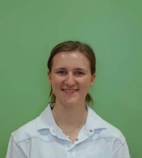 Porträt einer lächelnden Frau mit hellblauem Hemd vor grünem einfarbigem Hintergrund, zentriert aufgenommen.