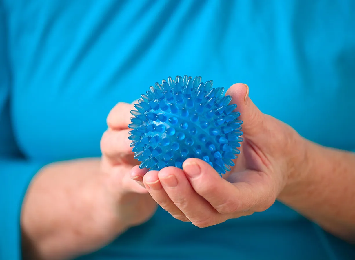 Blaues, stacheliges Massageball in den Händen einer Person, die ein türkisfarbenes Oberteil trägt.