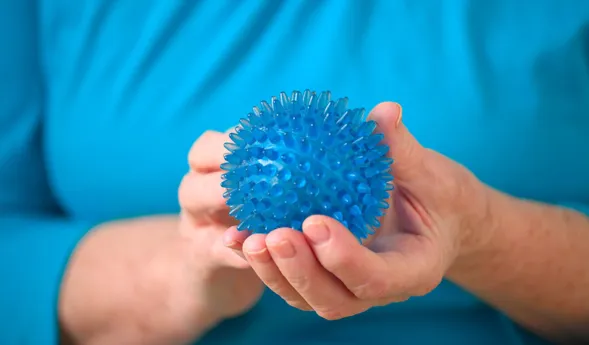 Blaues, stacheliges Massageball in den Händen einer Person, die ein türkisfarbenes Oberteil trägt.