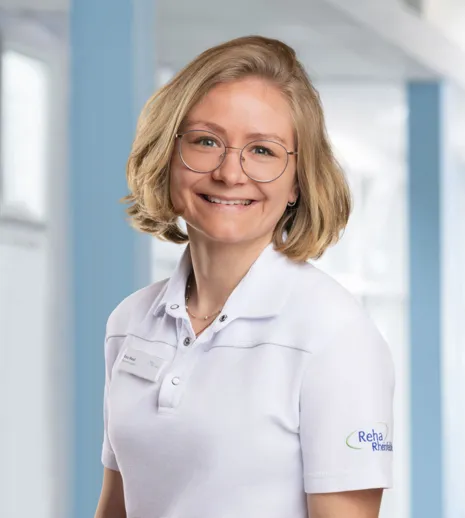 Porträt einer freundlichen Frau mit kurz blondem Haar und Brille im weißen Firmen-Poloshirt vor hellem blau-weißen Hintergrund.