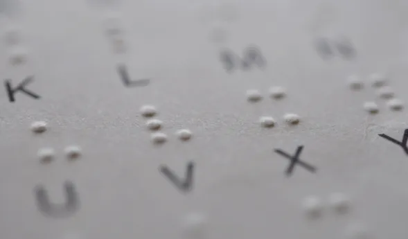 Braille-Schrift auf einem Blatt Papier mit erhabenen Punkten und gedruckten Buchstaben, darunter die Buchstaben K, L, M, N, U, V und X.