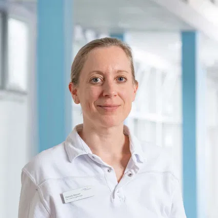 Porträt einer Frau im weißen Hemd in einem Büro mit blauen Elementen, freundlich in die Kamera lächelnd.