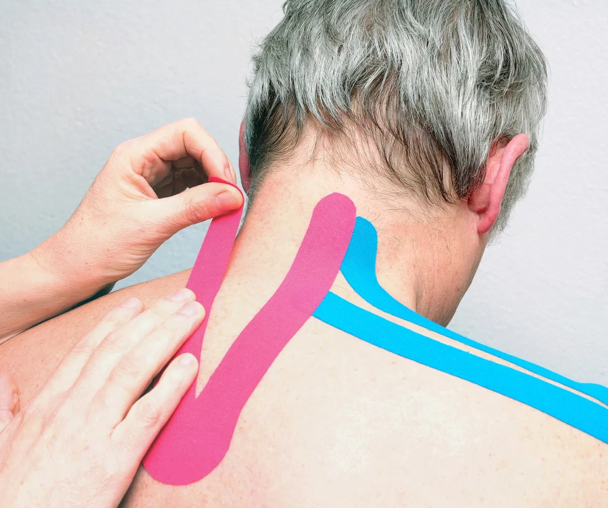 Person erhält pinke und blaue Kinesio-Tapes am Nacken und oberen Rücken.