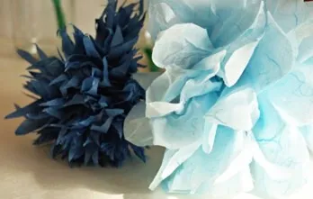 Blauer und hellblauer Papierblumenstrauß mit großen gefalteten Blütenblättern, dekorativ vor neutralem Hintergrund.