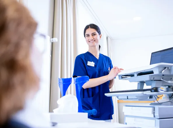 Krankenschwester in blauer Dienstkleidung an einem modernen Drucker/Scanner in einem Büro, bedient ein Gerät vor weißem Hintergrund mit Vorhang und Vorhängen im Hintergrund.