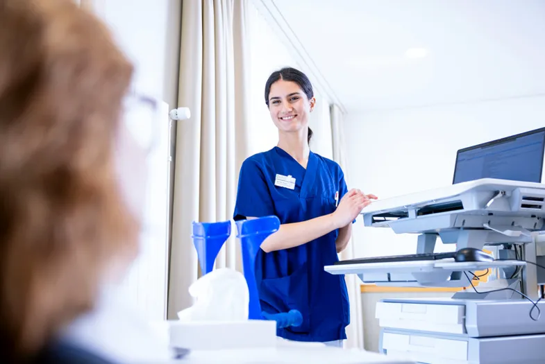 Krankenschwester in blauer Dienstkleidung an einem modernen Drucker/Scanner in einem Büro, bedient ein Gerät vor weißem Hintergrund mit Vorhang und Vorhängen im Hintergrund.