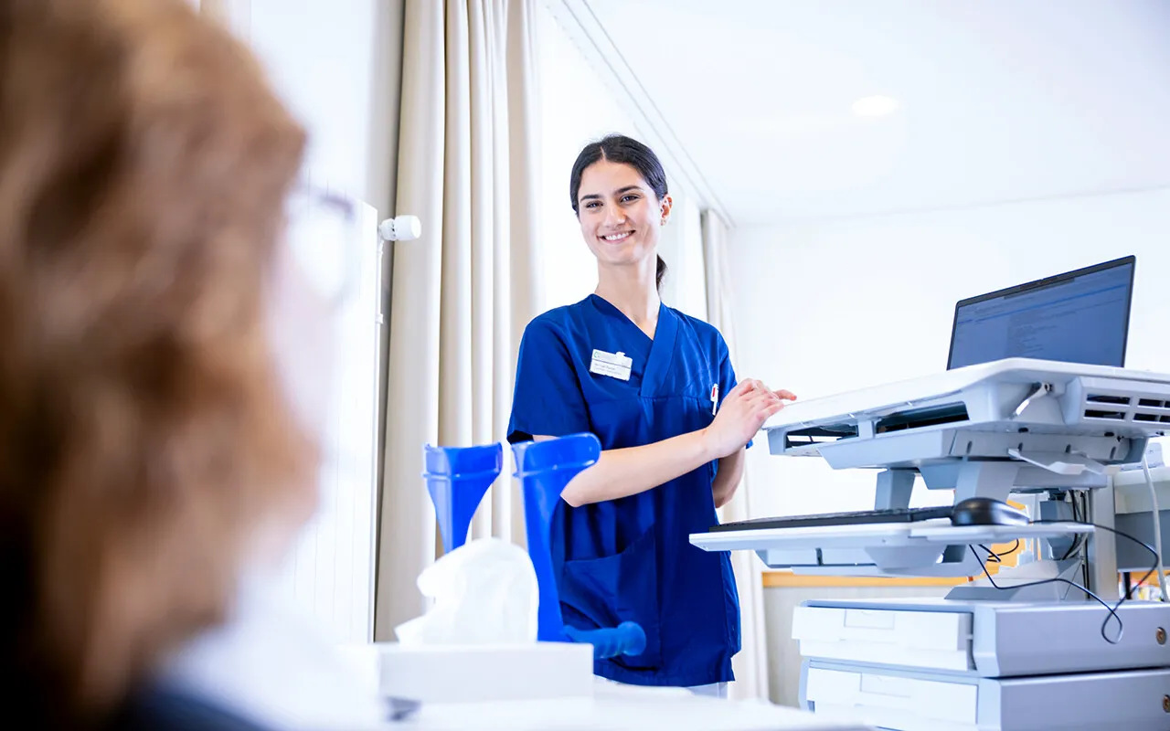 Krankenschwester in blauer Dienstkleidung an einem modernen Drucker/Scanner in einem Büro, bedient ein Gerät vor weißem Hintergrund mit Vorhang und Vorhängen im Hintergrund.