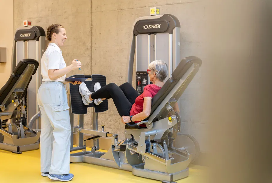 Trainerin betreut ältere Frau beim Beintraining an einem Cybex-Fitnessgerät im Trainingsraum.