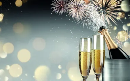 Champagnerflasche in einem Eiskübel, zwei Sektgläser mit prickelndem Inhalt, im Hintergrund Feuerwerkskörper und verschwommene Lichter.