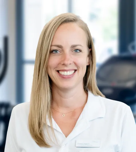 Lächelnde blonde Frau im weißen Kittel, Porträt vor unscharfem Fitnessstudio mit Trainingsgeräten, helles Hintergrundlicht.