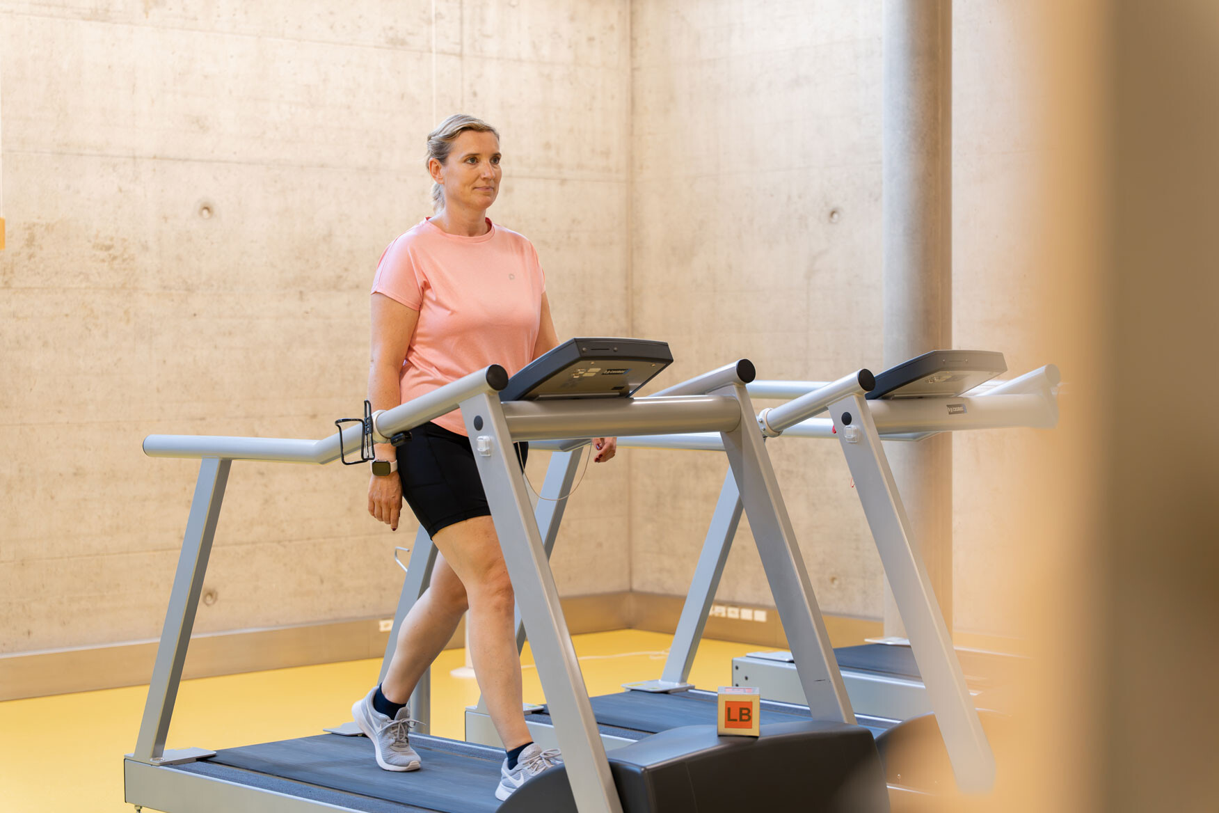 Frau in rosa Shirt geht auf einem Laufband in einem hellen Fitnessraum.