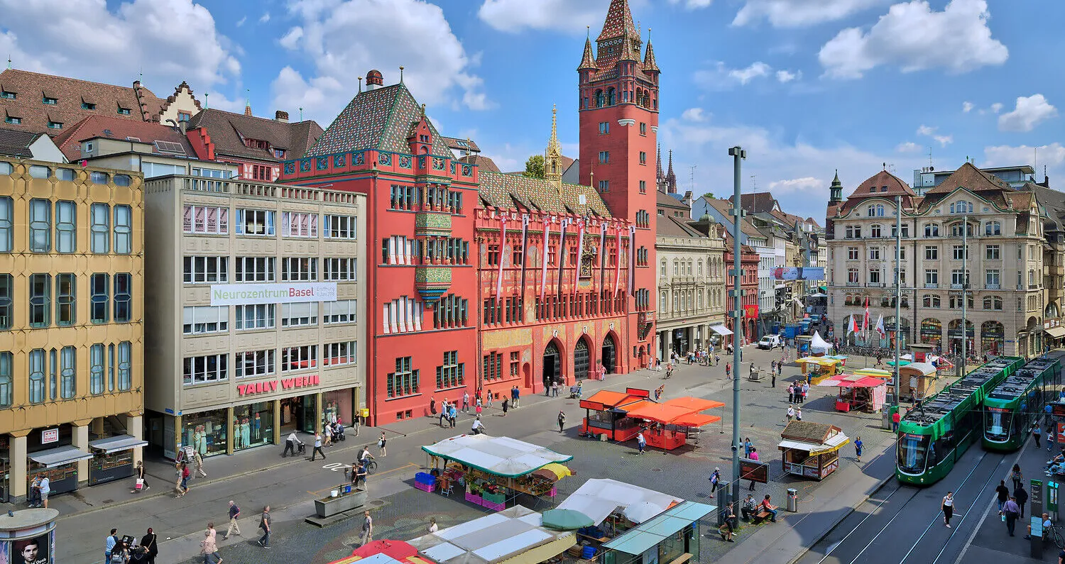 Der imposante Turm, die rote Fassade, und die verspielten Fassadenmalereien machen das Basler Rathaus zu einem Wahrzeichen der Stadt. Davor bietet der Stadtmarkt frisches Obst und Gemüse, Kräuter, Blumen, und andere lokale Erzeugnisse. // The Town hall...