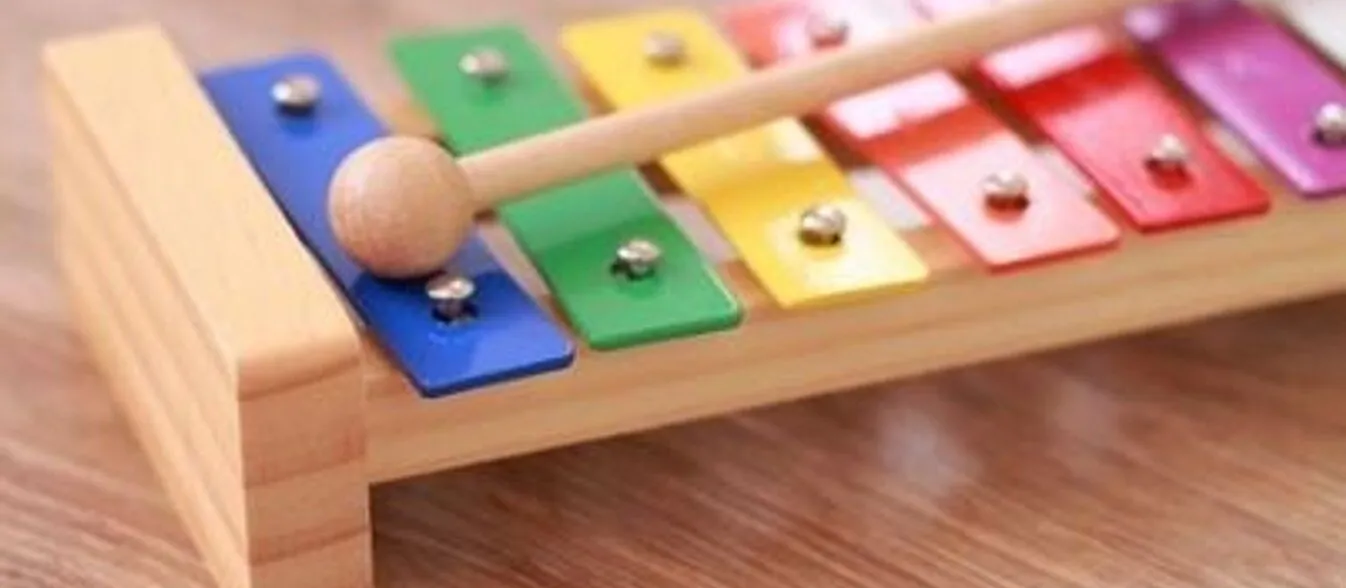 Buntes Xylophon mit mehreren farbigen Klangplatten und einem Holzschlägel auf einem Holzuntergrund.