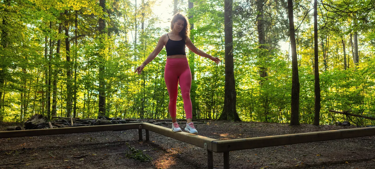 Eine Fau blanceiert über einen Holzbalken. dies ist ein Teil vom 
Vitaparcours Baden