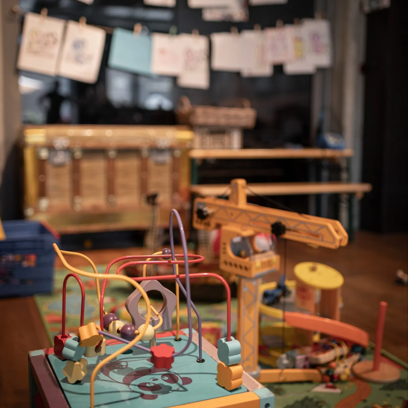 Bunter Kinderspielbereich mit Motorikspielzeug, Holzkran, Spielteppich und an einer Schnur aufgehängten Kinderzeichnungen.